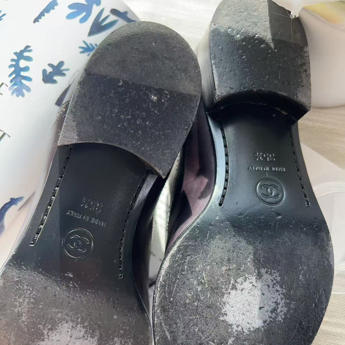 A pair of black Chanel shoes shown from the sole side, revealing heavy white powder or dust buildup on the soles. The Chanel logo and size '39' are visible on the insoles.