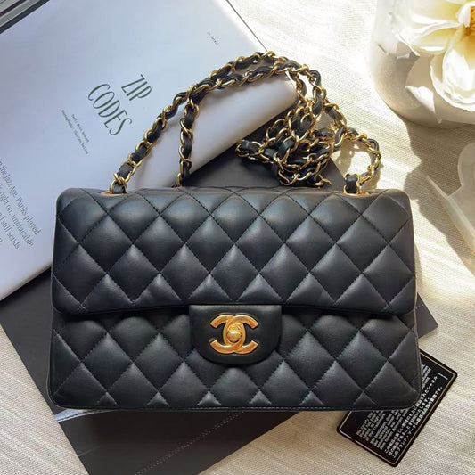 A black quilted leather shoulder bag with a gold-tone interlocking CC clasp, resting on a white magazine and a dark box with a gold chain strap.