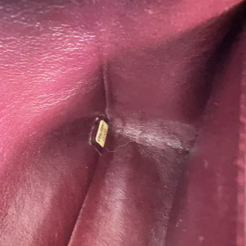 Close-up of a burgundy leather interior pocket showing a small gold-toned metal tag attached to the lining.