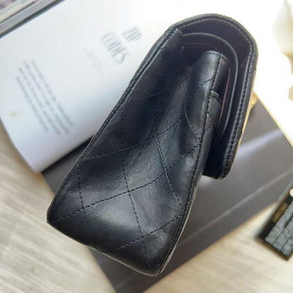 A black quilted leather wallet or card case with a triangular pointed end, photographed on top of a white book and a dark box on a light wood surface.