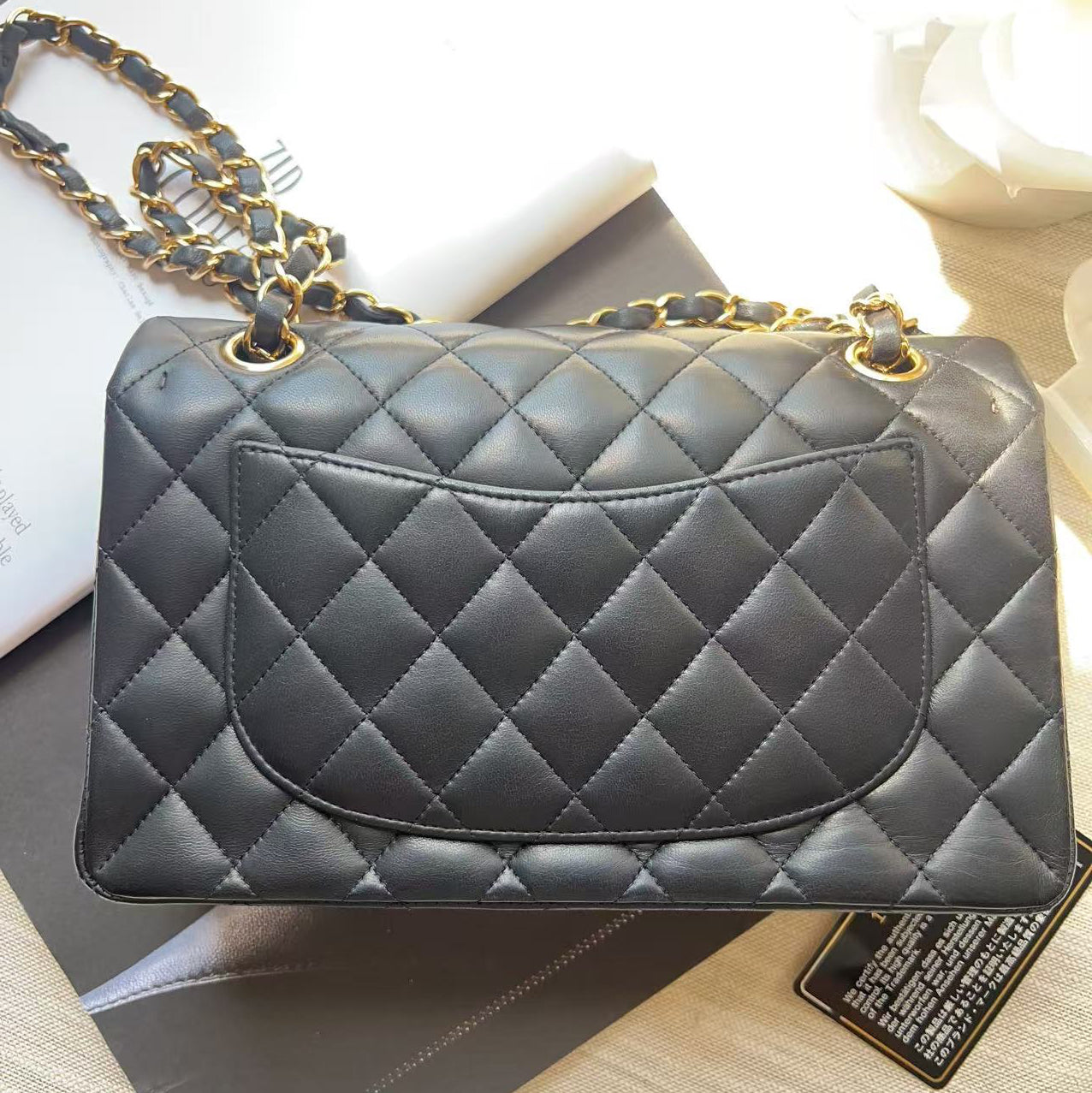 A black quilted leather handbag with gold-tone chain detailing, displayed on top of a dark box and white papers.