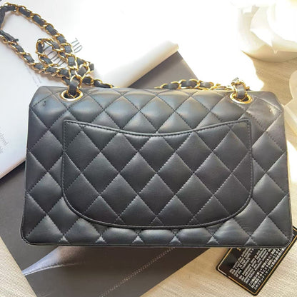 A black quilted leather handbag with gold-tone chain detailing, displayed on top of a dark box and white papers.