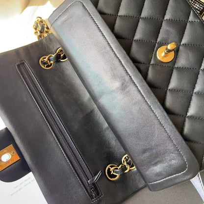 A close-up of a black leather shoulder bag with gold-tone hardware, showing the interior zipper pocket and flap, laid next to a quilted black bag on a light surface.