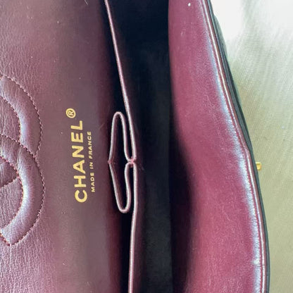 Close-up of a Chanel handbag interior in burgundy leather, showing the gold-embossed CHANEL logo and a finger holding the open flap.