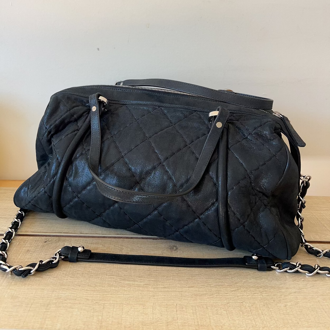 Black quilted handbag with chain detail on a wooden surface