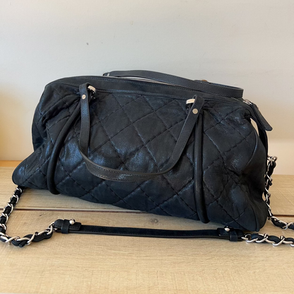 Black quilted handbag with chain detail on a wooden surface