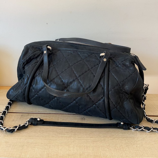 Black quilted handbag with chain detail on a wooden surface