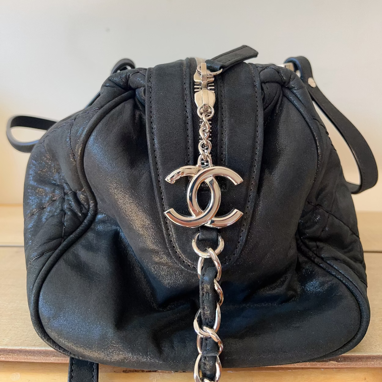 Black leather handbag with silver chain and CC logo on a light wooden surface.