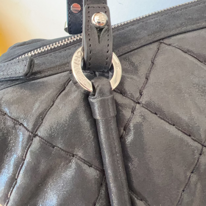 Close-up of a black quilted handbag with a strap and metal clasp.