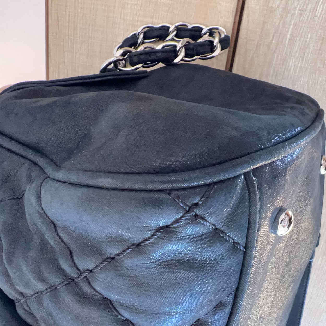 Black quilted handbag with a chain handle on a neutral background