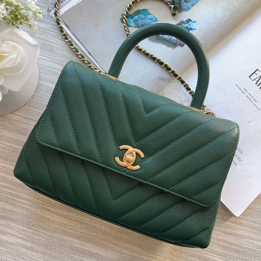 Green handbag with gold chain and clasp on a light wooden surface.