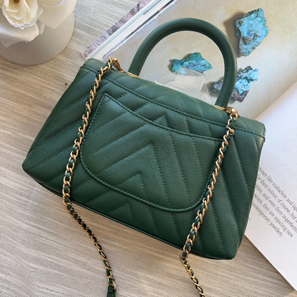 Green handbag with gold chain on a wooden surface with flowers and rocks in the background