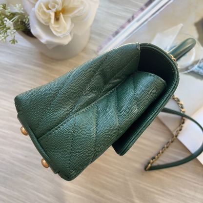 Green handbag with gold accents on a light wooden surface with flowers in the background