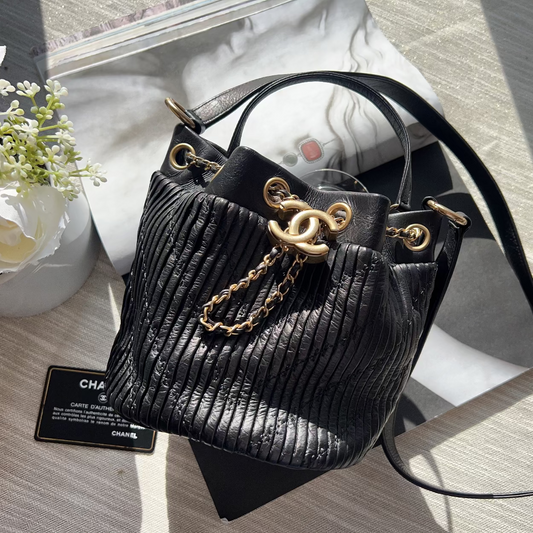 Black handbag with gold chain detail on a wooden surface with flowers and a card in the background