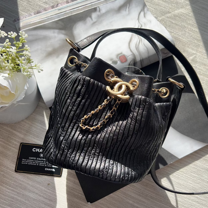 Black handbag with gold chain detail on a wooden surface with flowers and a card in the background