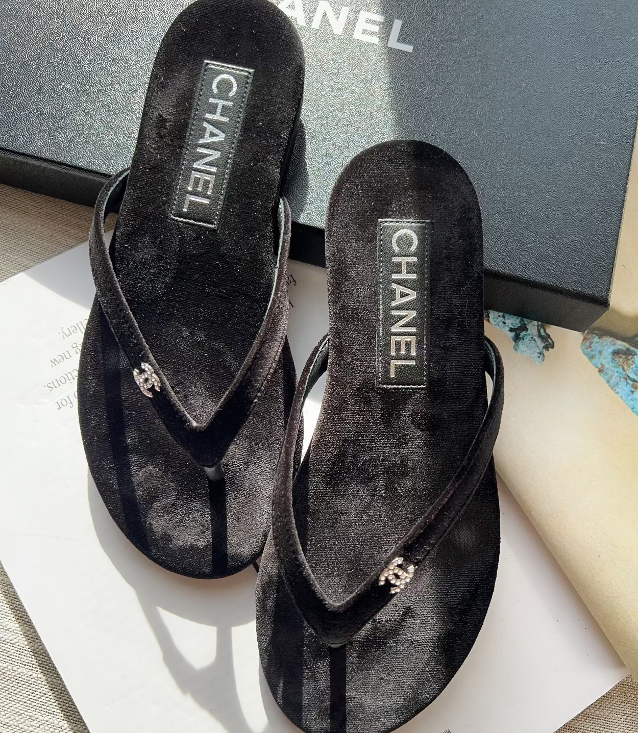 Black Chanel sandals on a white surface with a blurred background