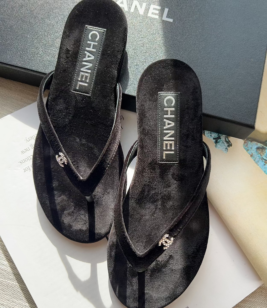 Black Chanel sandals on a white surface with a blurred background