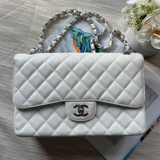 White quilted handbag with silver chain strap on a wooden surface with flowers.