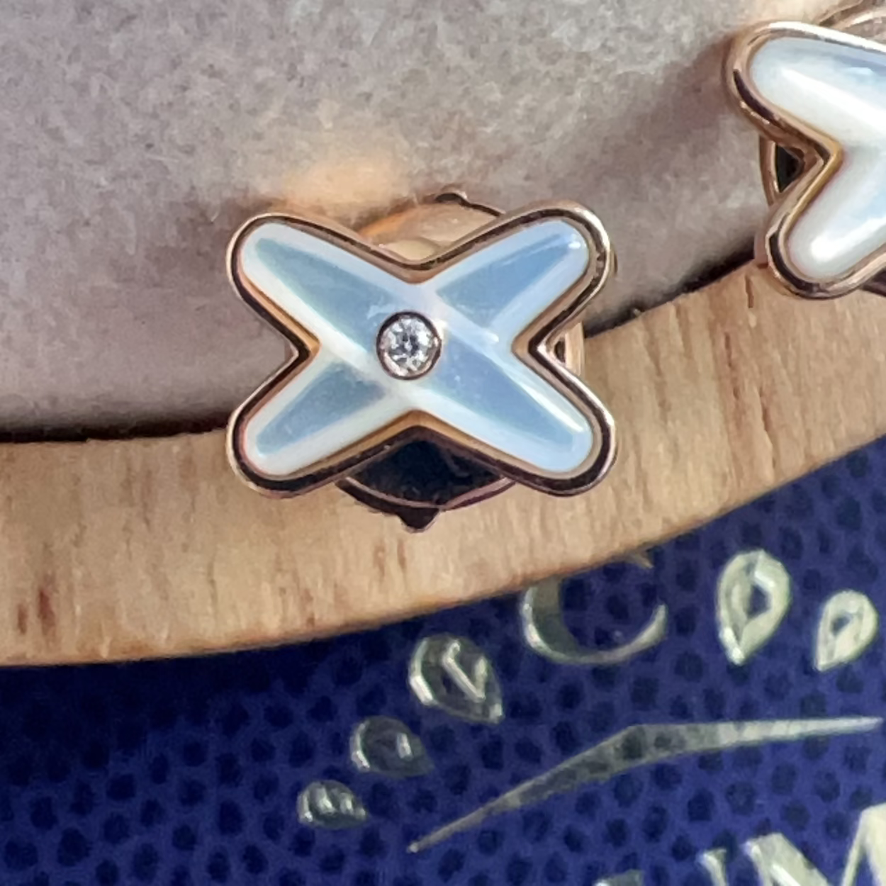 Close-up of a decorative 'X' charm on a textured surface with a visible brand name.