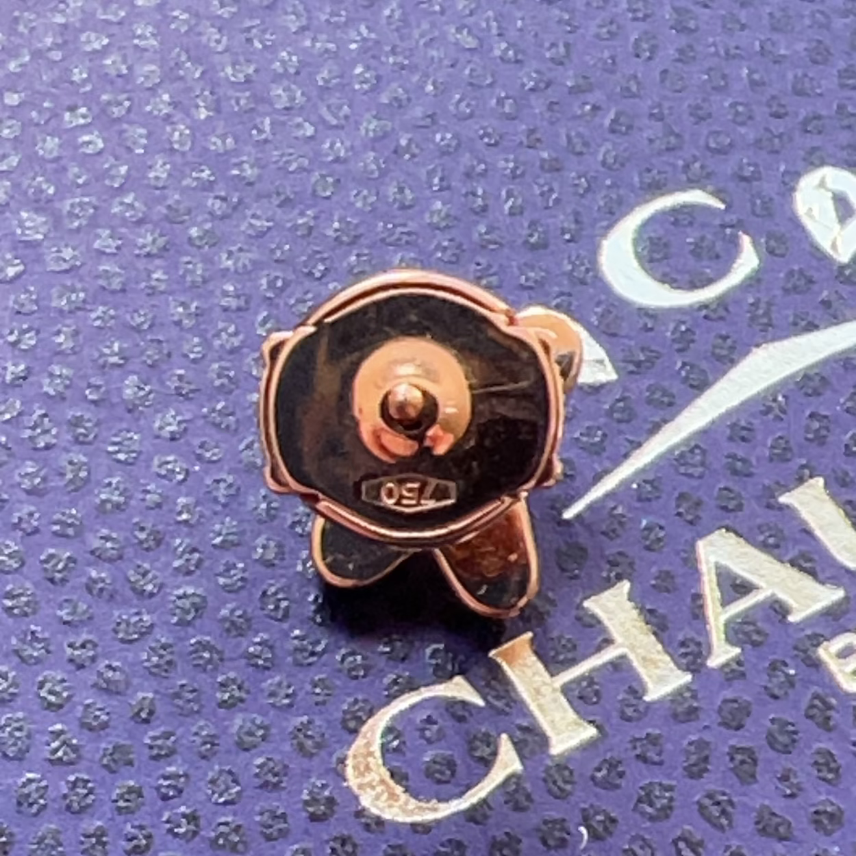 Rose gold and black earring on a purple textured surface with 'Chanel' branding.