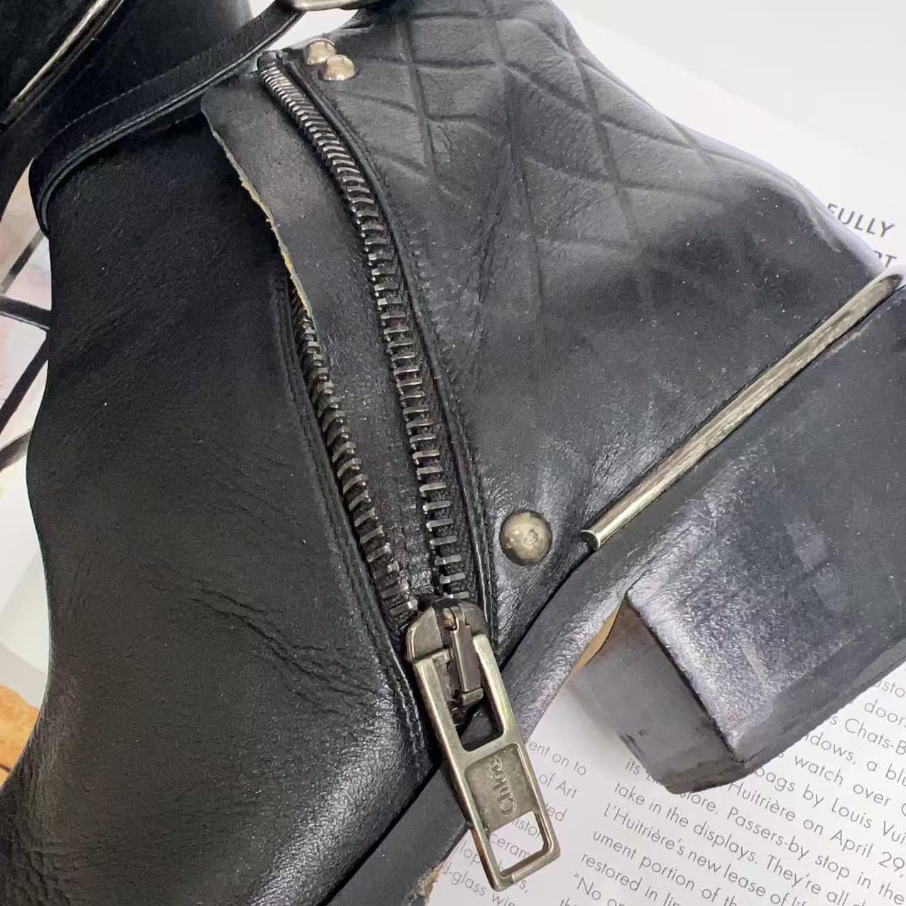 Close-up of a black leather boot with a zipper on a white surface.