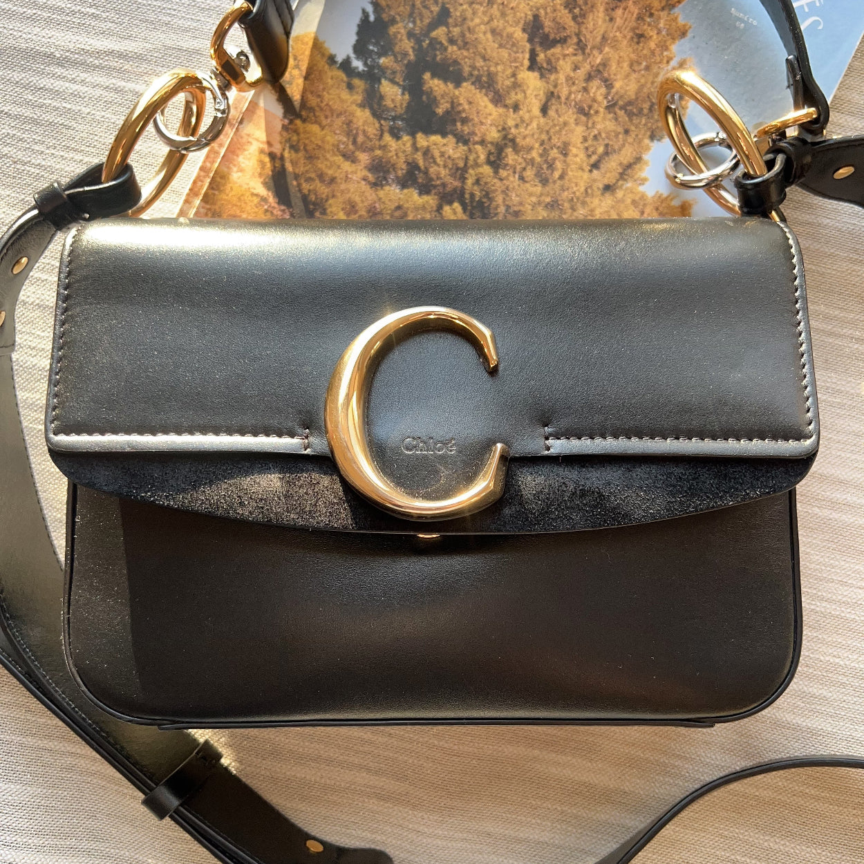 Black handbag with gold clasp on a light wooden surface