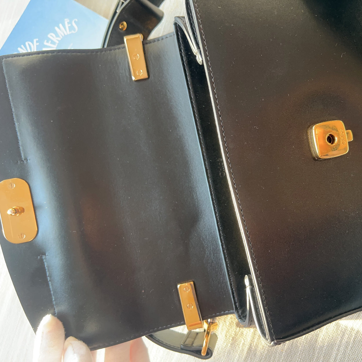 Black leather handbag with gold accents held by a hand on a light background