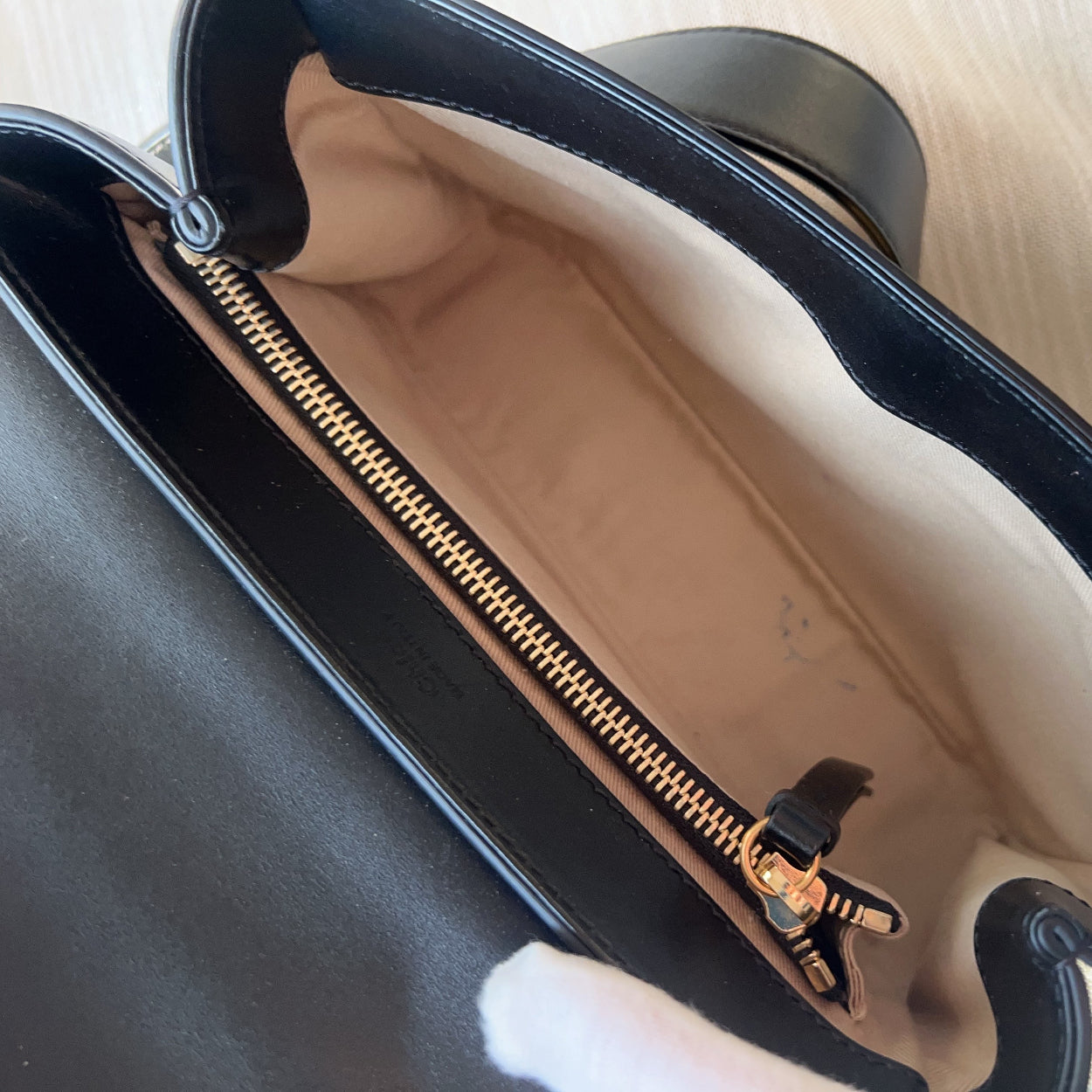 Close-up of a black handbag with a gold zipper, held by a gloved hand.