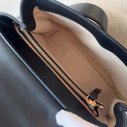 Close-up of a black handbag with a gold zipper, held by a gloved hand.