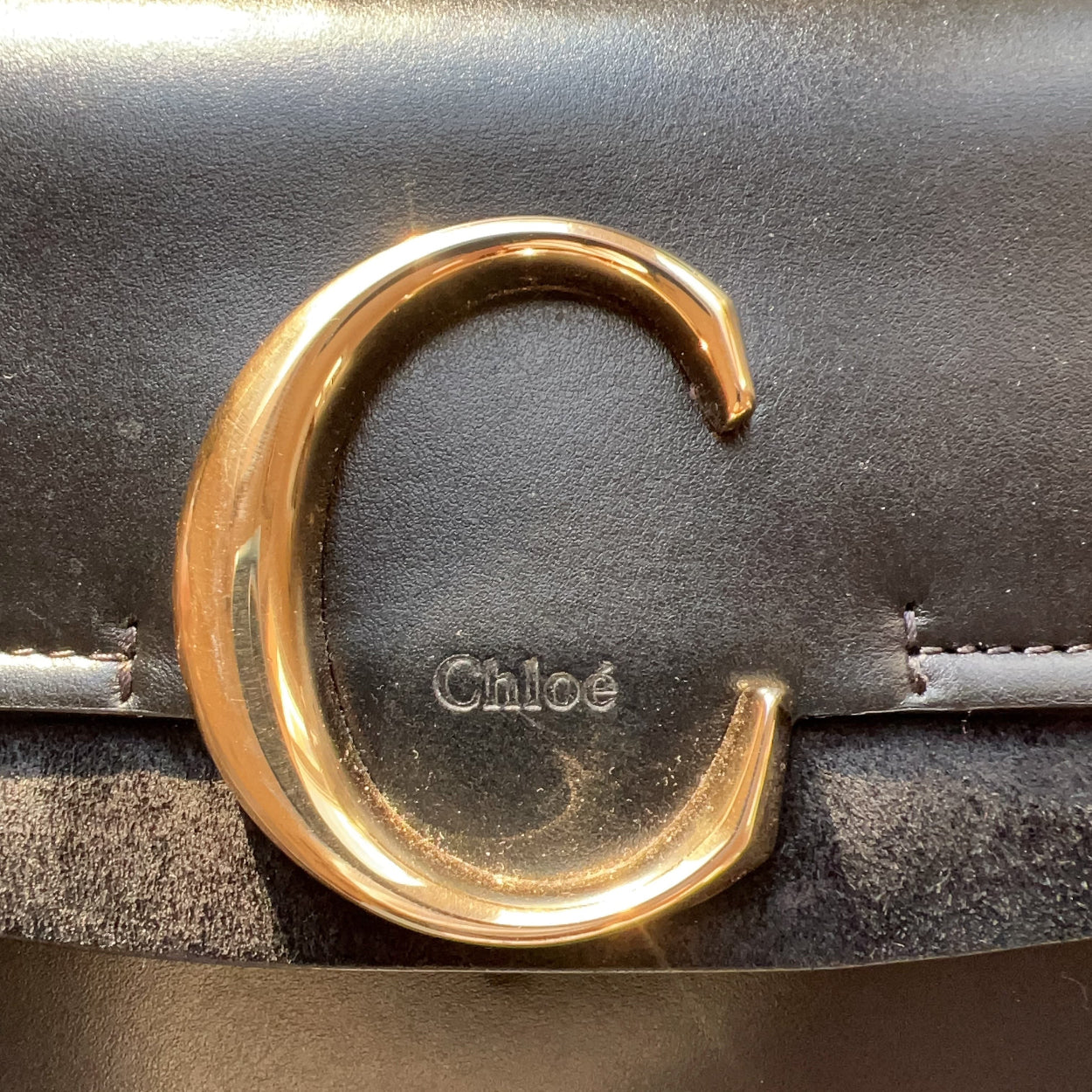 Close-up of a gold belt buckle on a leather belt with 'Chloe' branding.