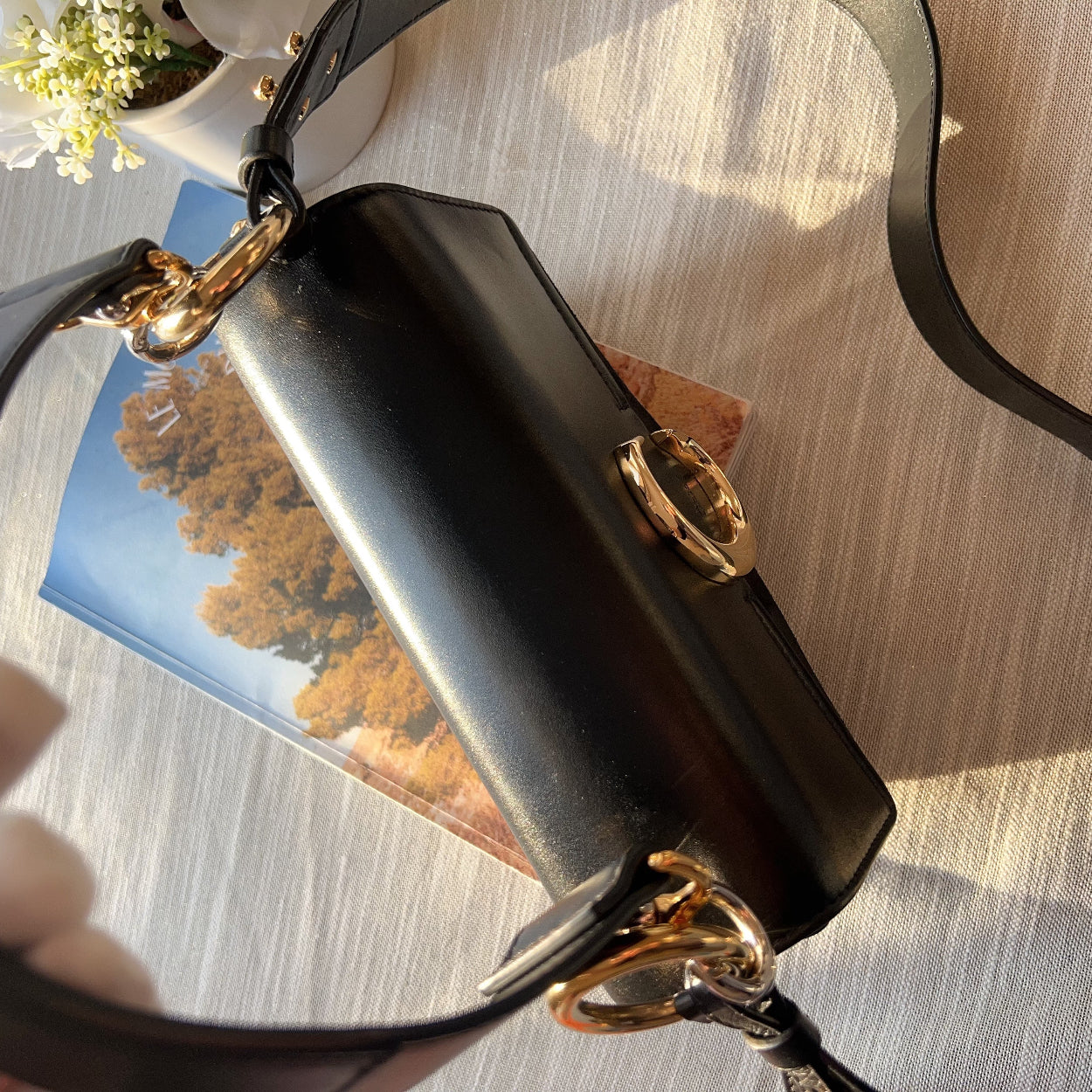 Black handbag with gold accents held by a hand on a reflective surface.