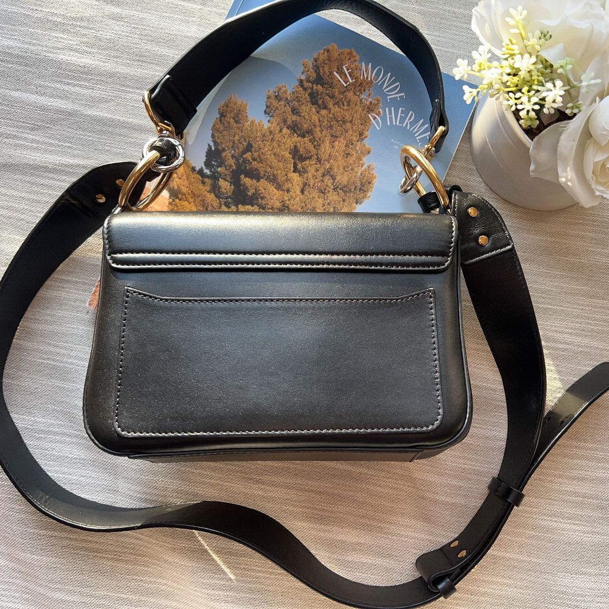 Black handbag on a wooden surface with flowers in the background