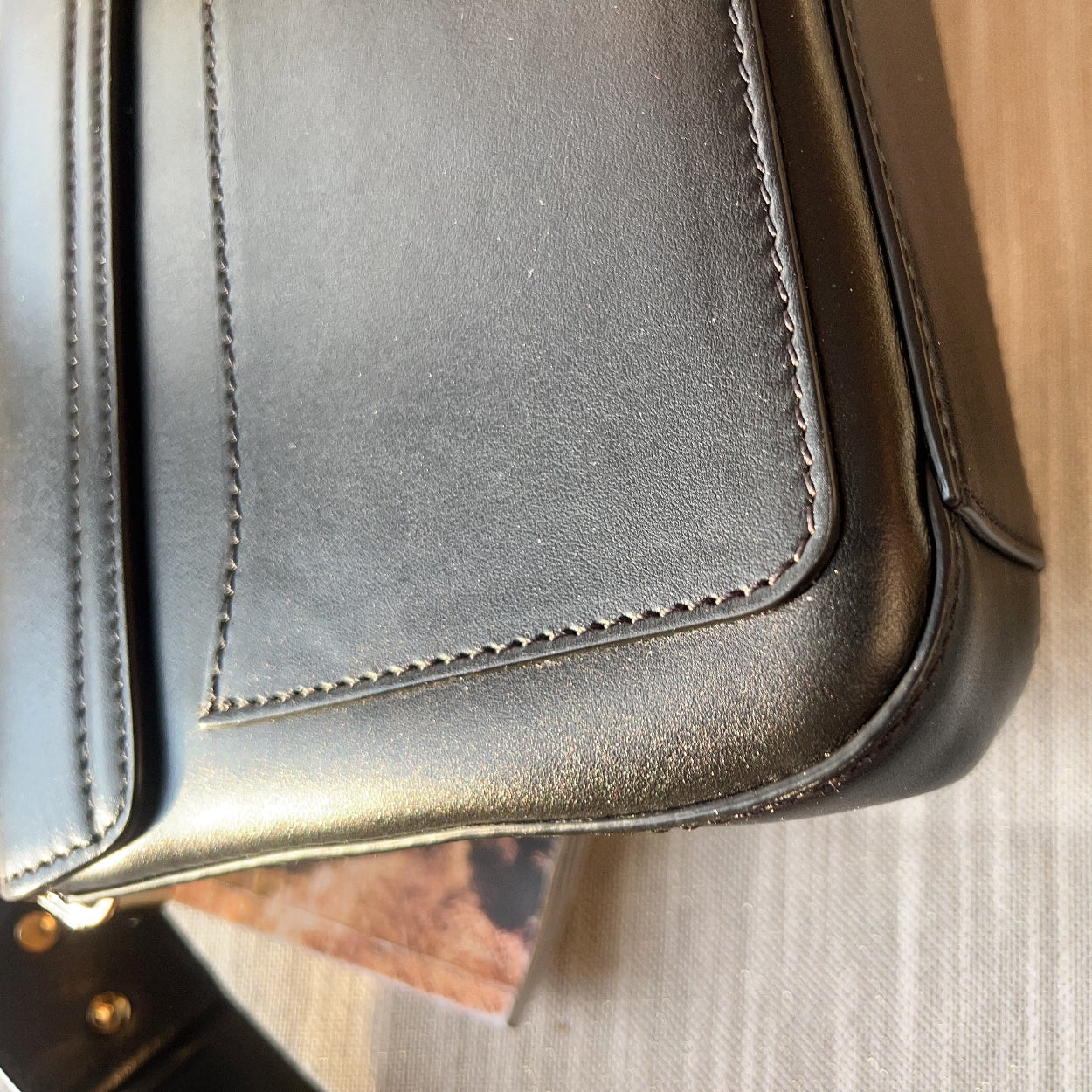 Close-up of a black leather bag with visible stitching on a wooden surface.