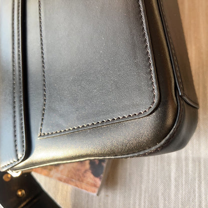 Close-up of a black leather bag with visible stitching on a wooden surface.