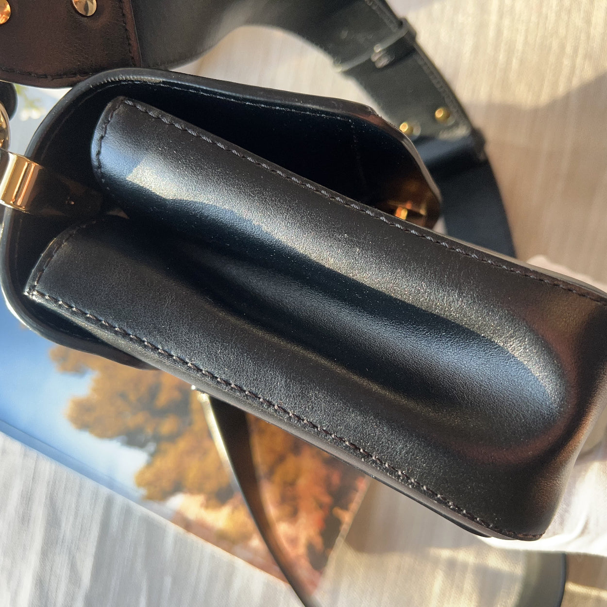 Close-up of a black leather handbag with a gold clasp on a textured surface.