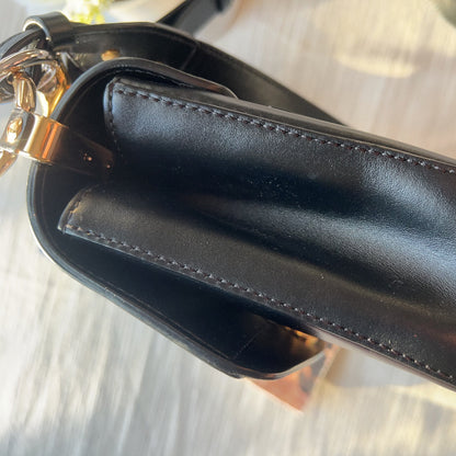 Close-up of a black leather handbag with a gold chain on a light background