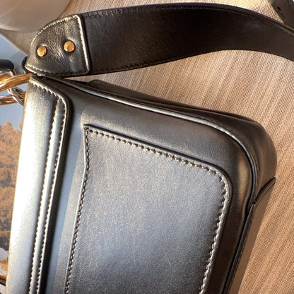 Close-up of a black leather bag with gold hardware on a wooden surface