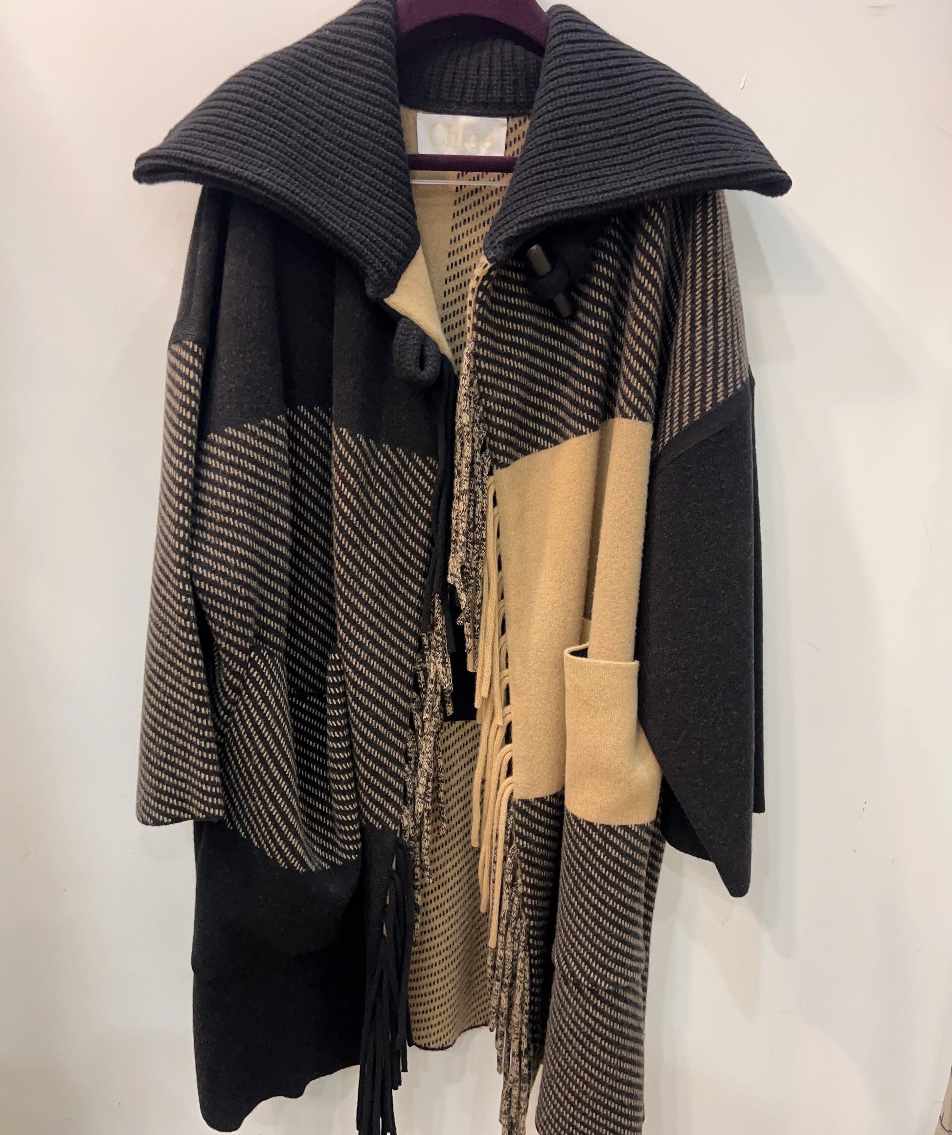 Hooded coat with black and beige pattern on a hanger against a white background