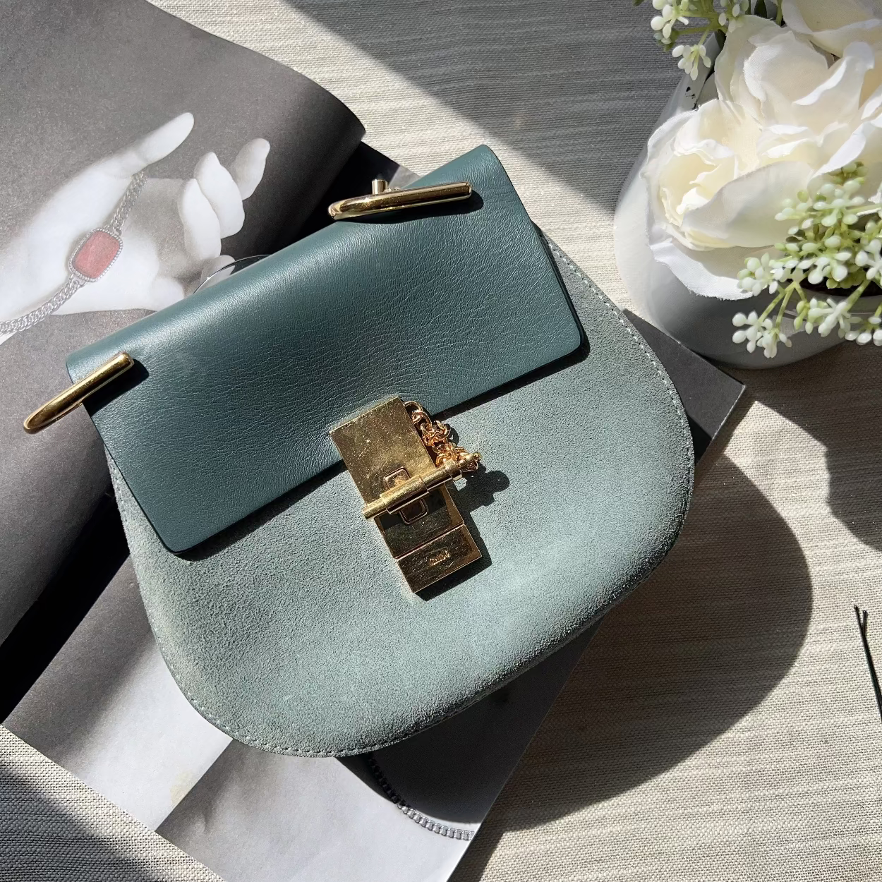 Green handbag with gold clasp on a textured surface with flowers in the background