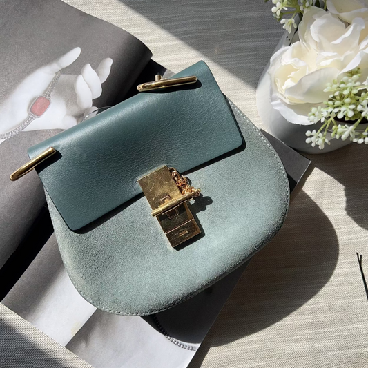 Green handbag with gold clasp on a textured surface with flowers in the background