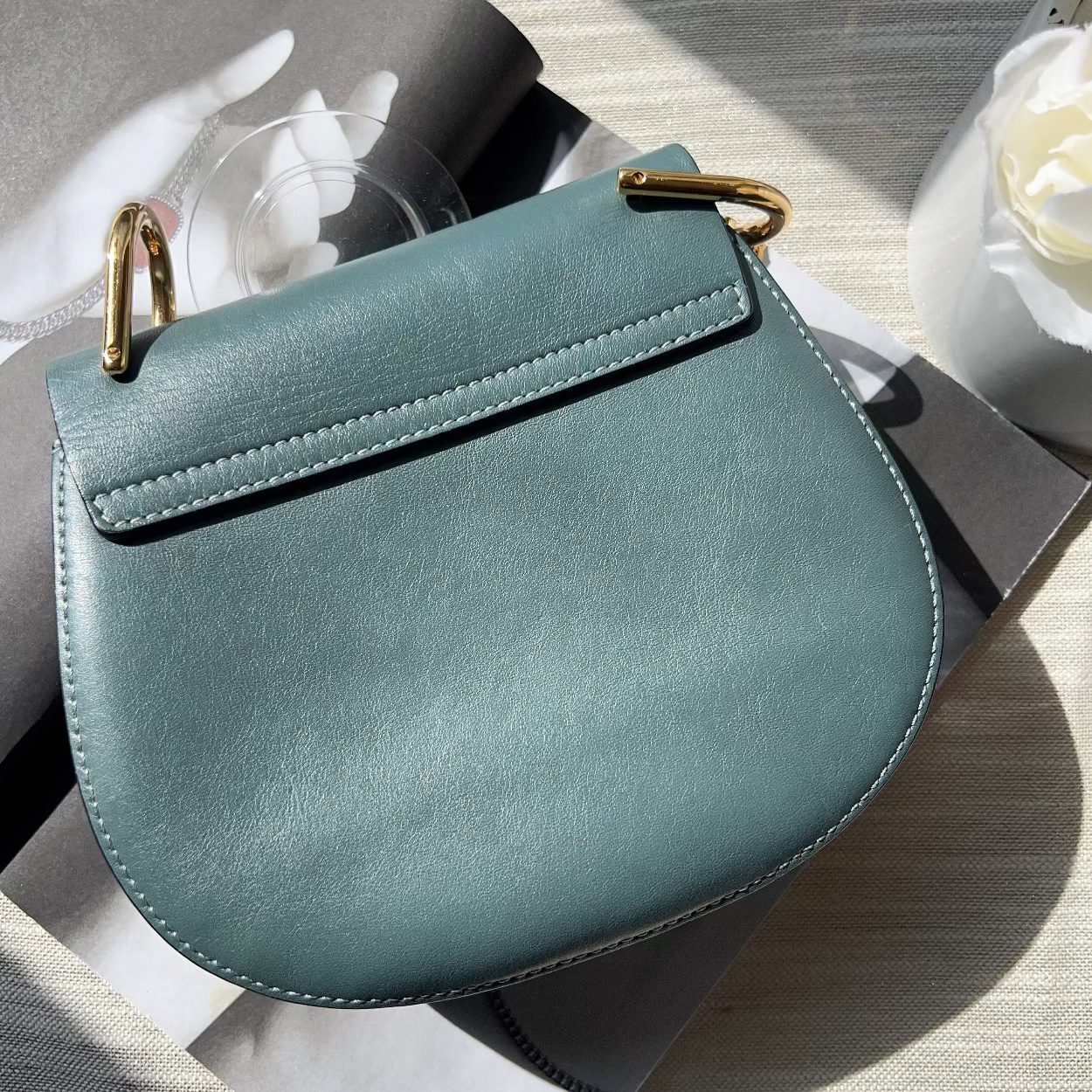 Teal handbag with gold accents on a light wooden surface