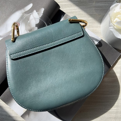 Teal handbag with gold accents on a light wooden surface