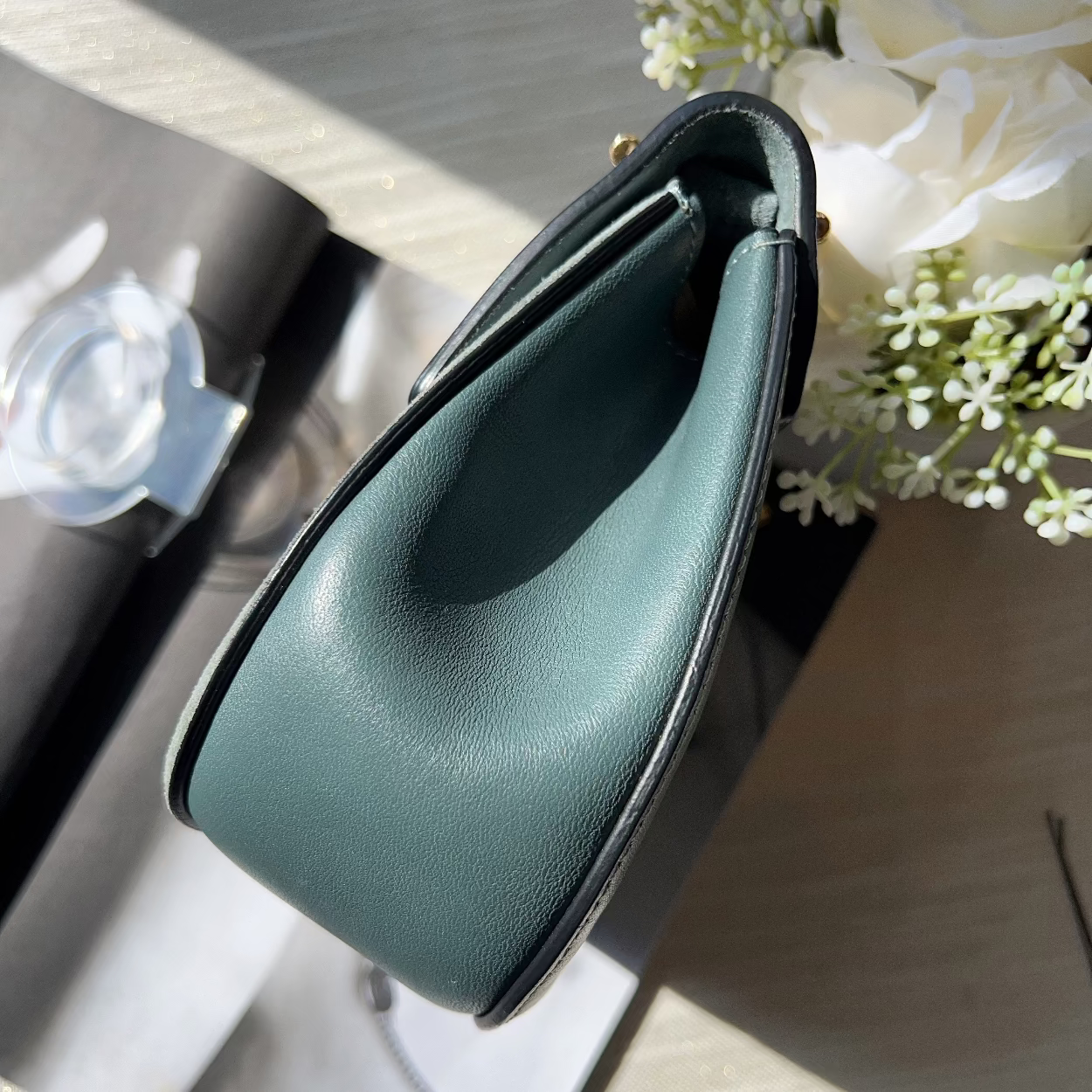 Green leather handbag on a wooden surface with flowers in the background