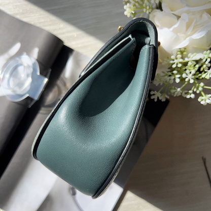 Green leather handbag on a wooden surface with flowers in the background