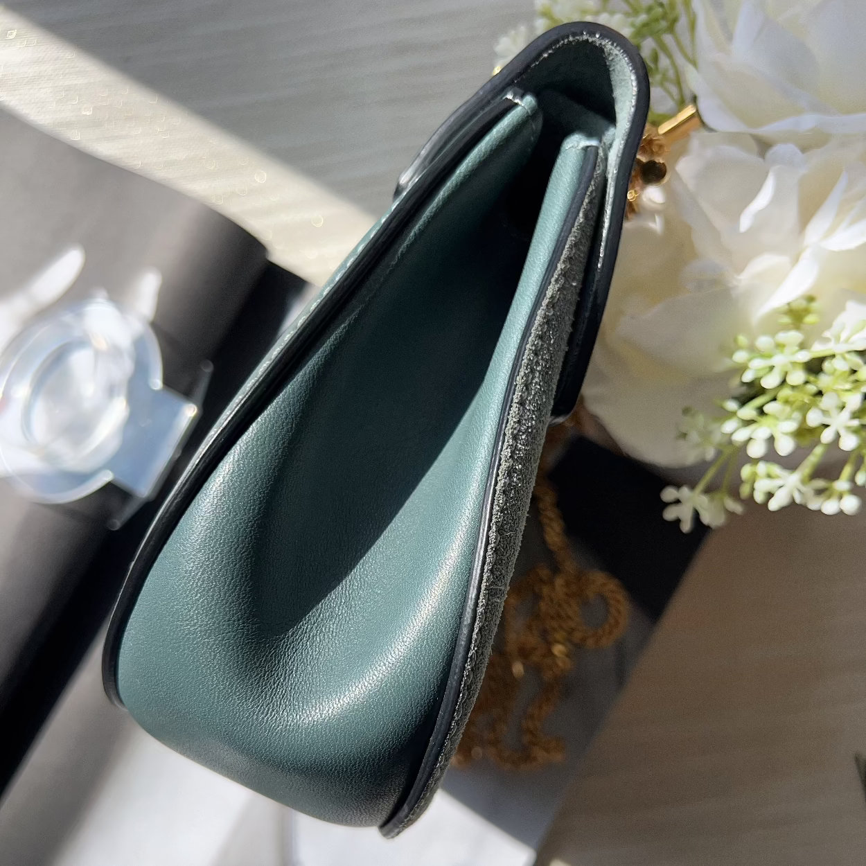Green leather clutch on a table with flowers in the background