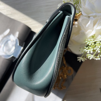 Green leather clutch on a table with flowers in the background