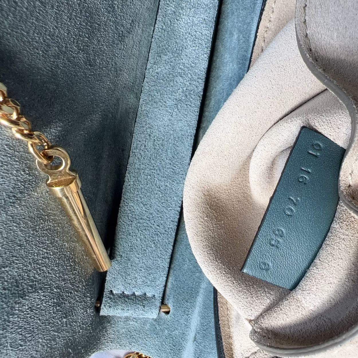 Close-up of a beige shoe with a blue insole tag, gold chain, and gray fabric background.
