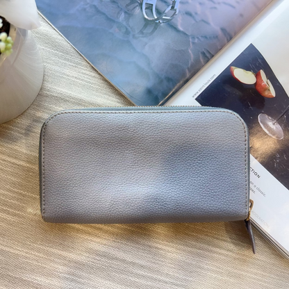 Gray wallet on a wooden surface with books and a plant in the background