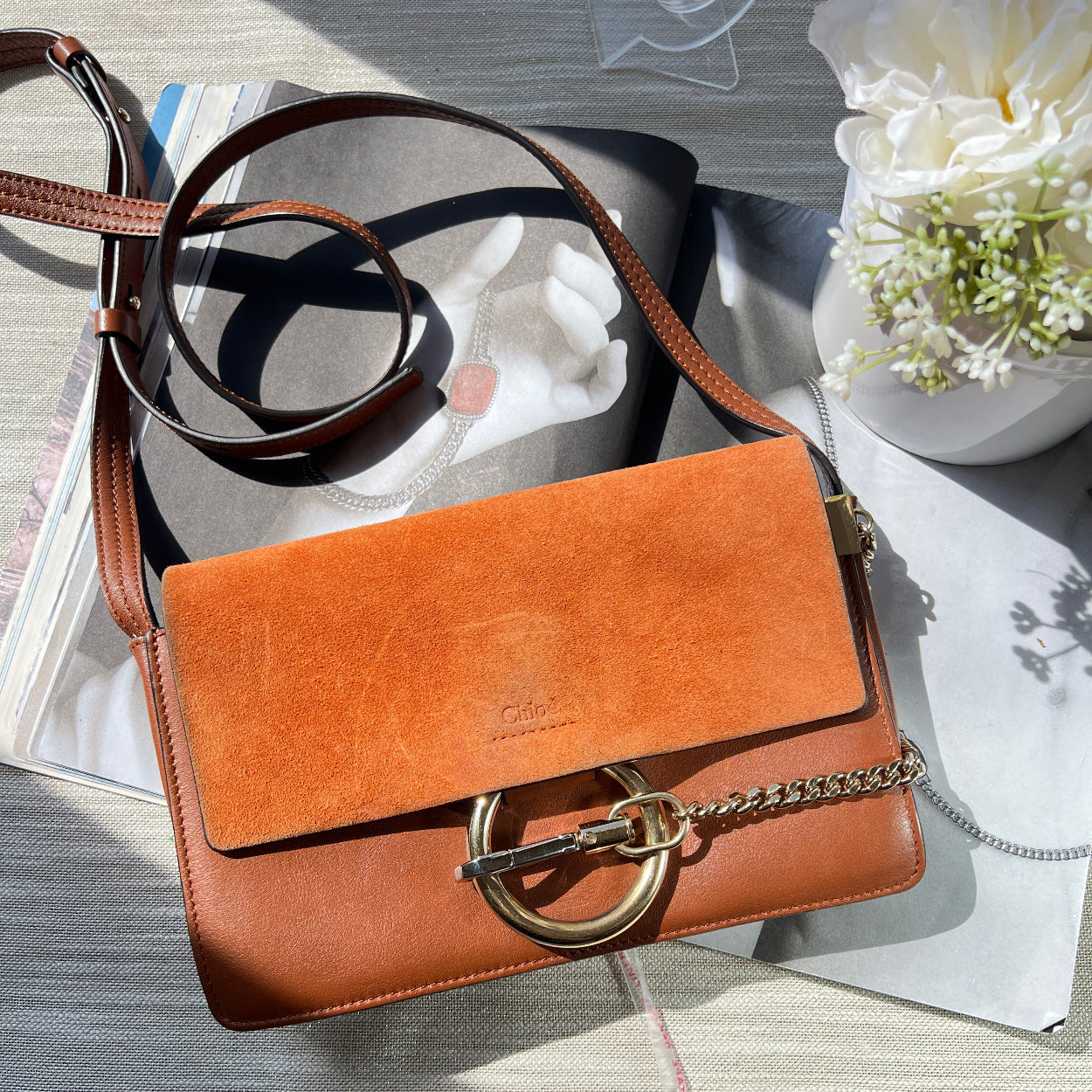 Brown leather handbag with a chain strap on a textured surface with flowers.