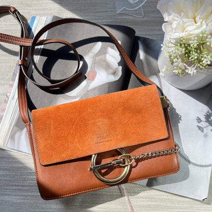 Brown leather handbag with a chain strap on a textured surface with flowers.